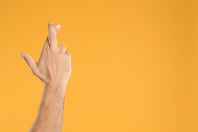 Man with crossed fingers and space for text on yellow background, closeup. Superstition concept