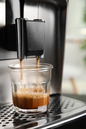 Photo of Espresso machine pouring coffee into glass against blurred background, closeup