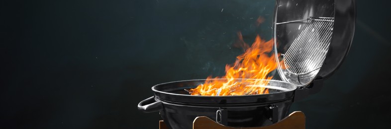 Image of New modern barbecue grill with burning firewood on dark background. Banner design