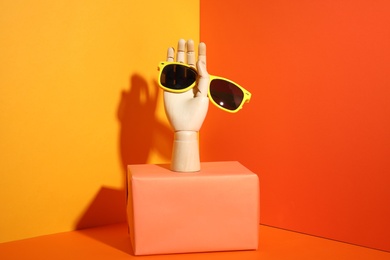 Wooden mannequin hand with stylish sunglasses on color background