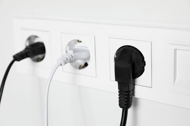 Power sockets with inserted plugs on white wall, closeup. Electrical supply