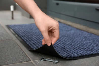 Woman's hand lifting door mat to reveal key hidden underneath, closeup