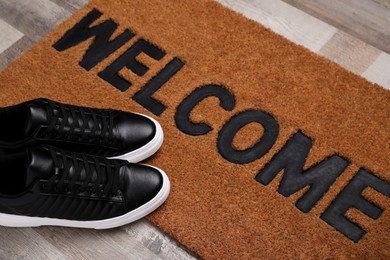New clean mat with word WELCOME and shoes on floor