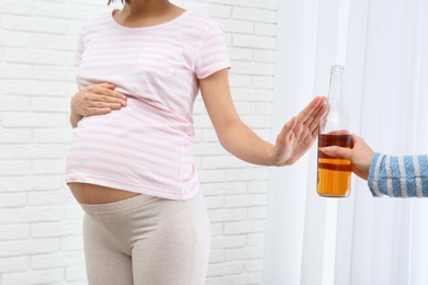 Pregnant woman declining whiskey indoors. Alcohol harm