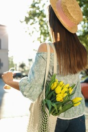 Photo of Young woman with bouquet of yellow tulips on city street, back view