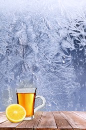 Cup of hot tea on wooden table near window covered with frost 