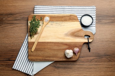 Photo of Cutting board and condiments on wooden table, flat lay. Cooking utensils
