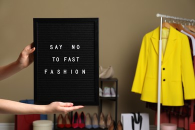 Woman holding black letter board with phrase SAY NO TO FAST FASHION indoors, closeup