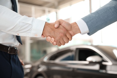 Photo of Young salesman shaking hands with client in modern car dealership, closeup