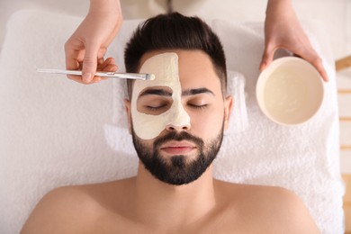 Cosmetologist applying mask on man's face in spa salon, top view