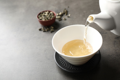 Pouring green tea into cup on grey table. Space for text