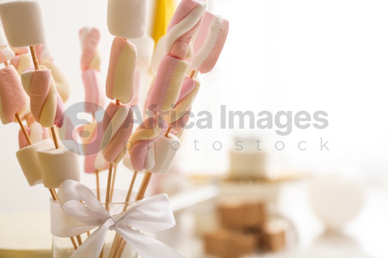 Tasty marshmallow on wooden sticks with bow in room decorated for birthday party, closeup