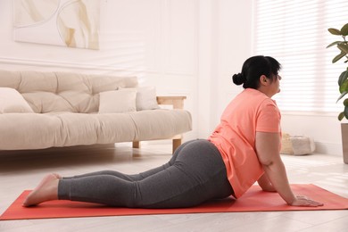 Overweight mature woman doing exercise on yoga mat at home