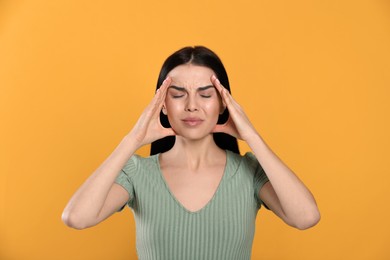 Woman suffering from migraine on yellow background