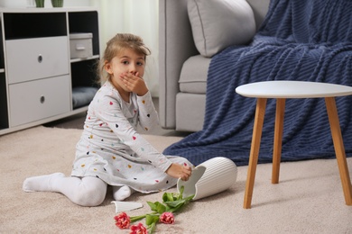 Emotional little girl and broken ceramic vase on floor at home