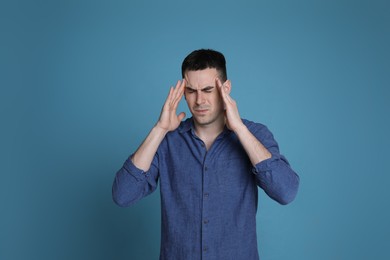 Young man suffering from headache on blue background, space for text. Cold symptoms