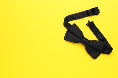 Stylish black bow tie on yellow background, top view. Space for text