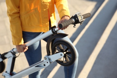 Woman carrying folded electric kick scooter outdoors, closeup