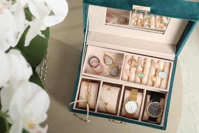 Elegant jewelry box with beautiful bijouterie and expensive wristwatches on beige table, top view
