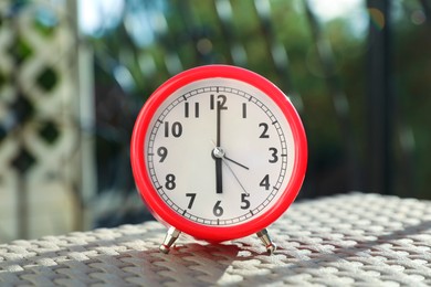 Photo of Red alarm clock on table outdoors at sunny morning
