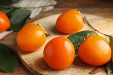 Delicious fresh persimmons and green leaves on wooden table, closeup