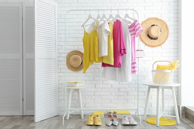 Wardrobe rack with women's clothes and different shoes at white brick wall in room
