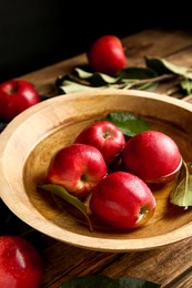 Ripe red apples in bowl of water on wooden table