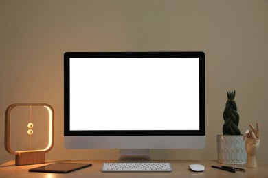Comfortable workplace with blank computer display on desk and plant near beige wall. Space for text