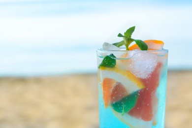Glass of refreshing drink with grapefruit and mint near sea, closeup. Space for text