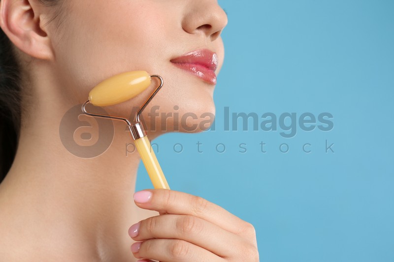 Photo of Woman using natural jade face roller on light blue background, closeup. Space for text