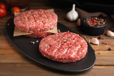 Raw hamburger patties with spices on wooden table