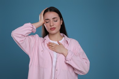 Young woman suffering from headache on blue background. Cold symptoms