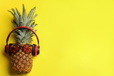 Photo of Top view of pineapple with sunglasses and headphones on yellow background, space for text. Creative concept