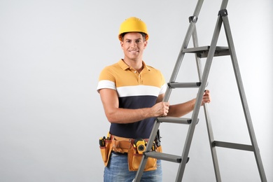 Professional builder with metal ladder on grey background