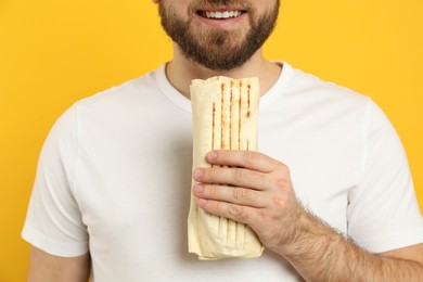 Photo of Young man with delicious shawarma on yellow background, closeup