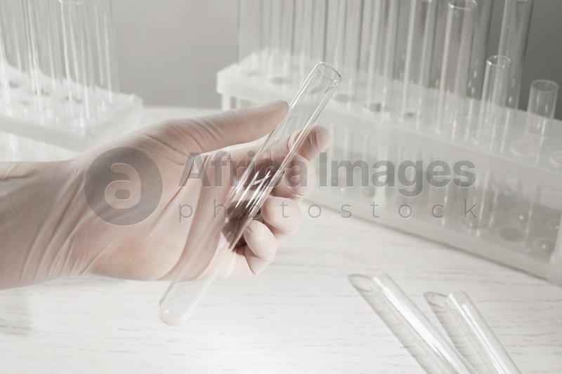 Scientist holding empty test tube at white table, closeup