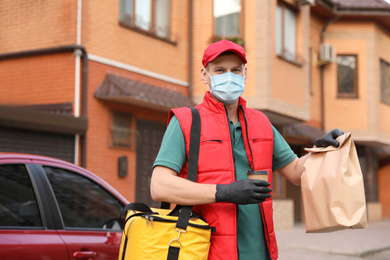 Courier in protective mask and gloves with orders near car outdoors. Food delivery service during coronavirus quarantine