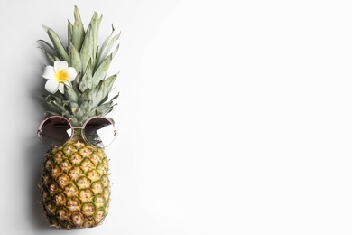 Photo of Pineapple with sunglasses and plumeria flower on white background, top view. Creative concept