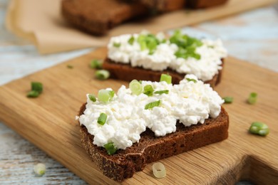 Photo of Bread with cottage cheese and green onion on light blue wooden table, closeup