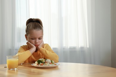 Cute little girl refusing to eat vegetable salad at home, space for text