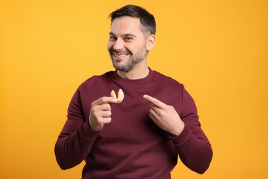 Photo of Happy man holding tasty fortune cookie with prediction on orange background