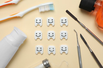 Plastic teeth with cute faces, oral care products and dental tools on beige background, flat lay