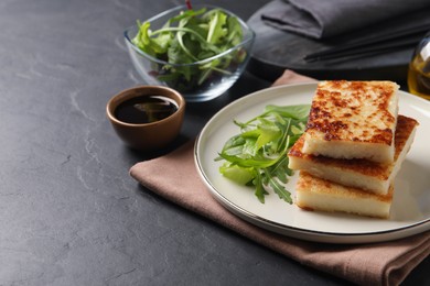 Photo of Delicious turnip cake with arugula served on black table. Space for text
