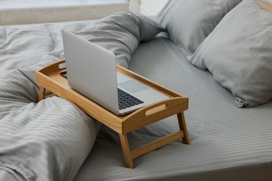 Wooden tray table with laptop on bed indoors