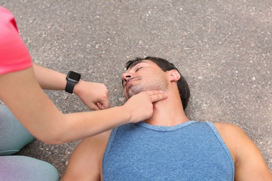 Young woman checking pulse of unconscious man on street
