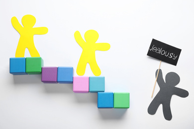 Human paper figures and stairs made of cubes on white background, flat lay. Concept of jealousy