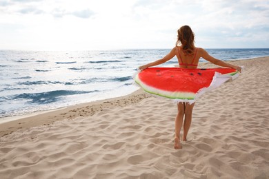 Beautiful woman with bright beach towel on seashore, back view