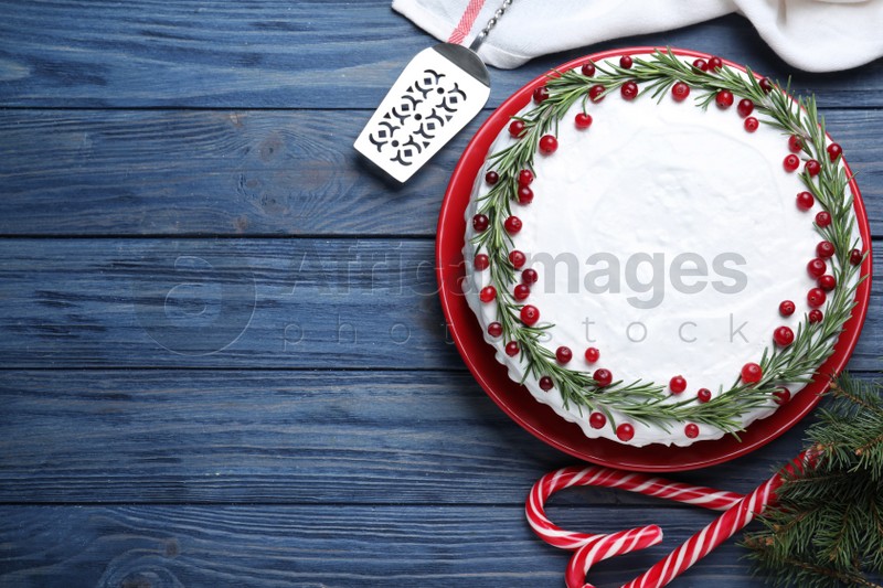 Photo of Traditional Christmas cake decorated with rosemary and cranberries on blue wooden table, flat lay. Space for text