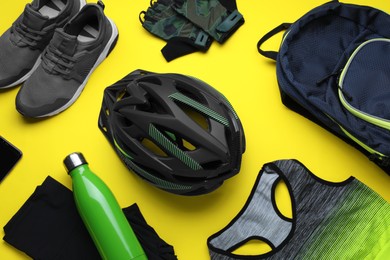 Flat lay composition with different cycling accessories and clothes on yellow background