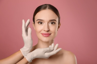 Doctor examining woman's face before plastic surgery on pink background